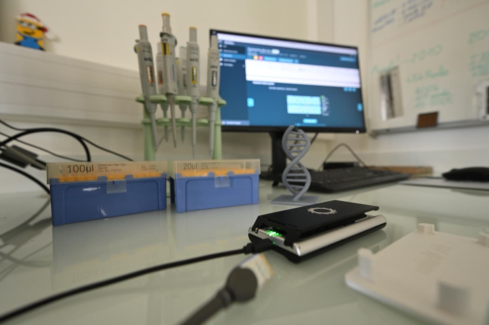 A DNA sequencer, pipettes, and instruments on a modern pharmaceutical and biotech research bench