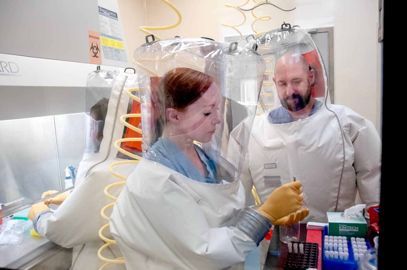 Scientists in biosafety suits working at a biosafety cabinet in a high-containment laboratory